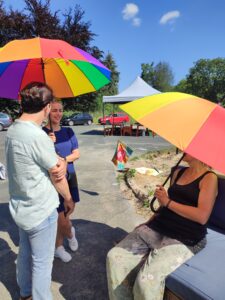 Das Schienenfest 2023. Menschen mit regenbogenfarbenen Sonnenschirmen. 