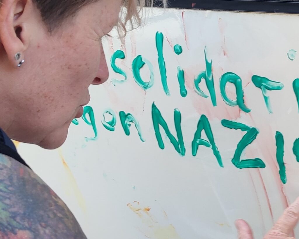 Das Foto zum Thema Antidiskriminierung / Antirassismus zeigt eine Frau die mit Fingerfarben "Solidarität gegen Nazis" an den Bus von Einsweiter schreibt. 