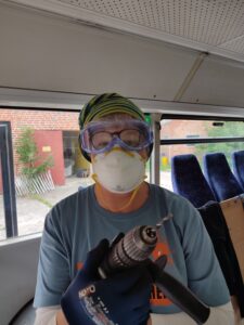 Rollstuhlgerechter Umbau von Bus "Bernhard". Ein*e Helfer*in mit Schutzbrille, Maske und Bohrmaschine "bewaffnet".